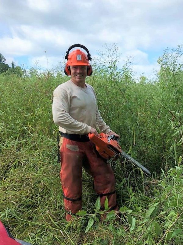 Sam Shoaf standing in a field holding a chainsaw.