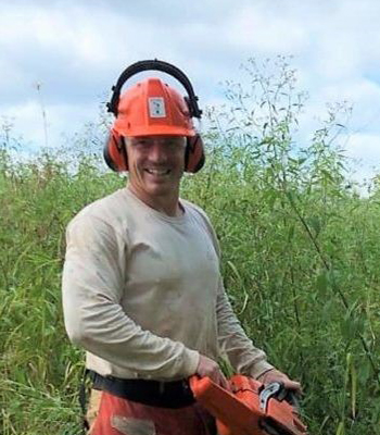 Sam Shoaf standing in field with chain saw.