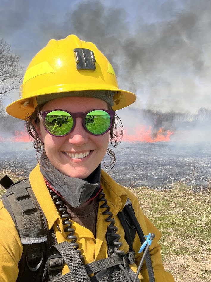 Danielle Howard in helmet and Nomex in front of fire